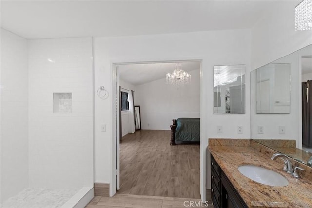 bathroom with a chandelier, a tile shower, vanity, and wood finished floors