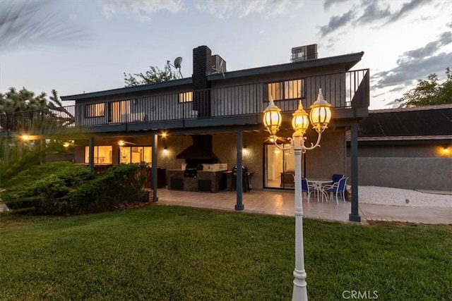 rear view of property featuring stucco siding, a lawn, and a patio