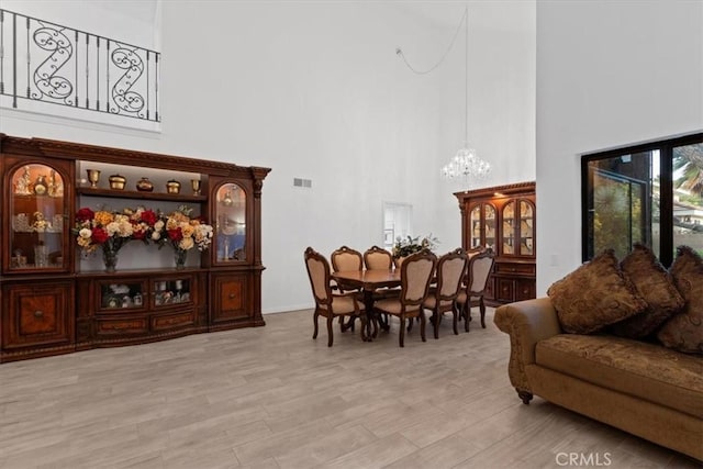 dining space featuring visible vents, a notable chandelier, light wood-style flooring, and a high ceiling