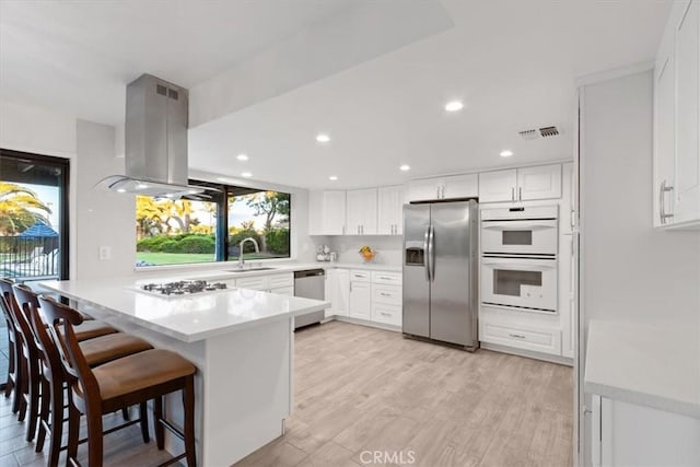 kitchen with visible vents, appliances with stainless steel finishes, a sink, island range hood, and a peninsula