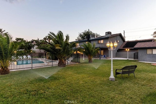 yard at dusk with central air condition unit, a patio area, fence, and a fenced in pool