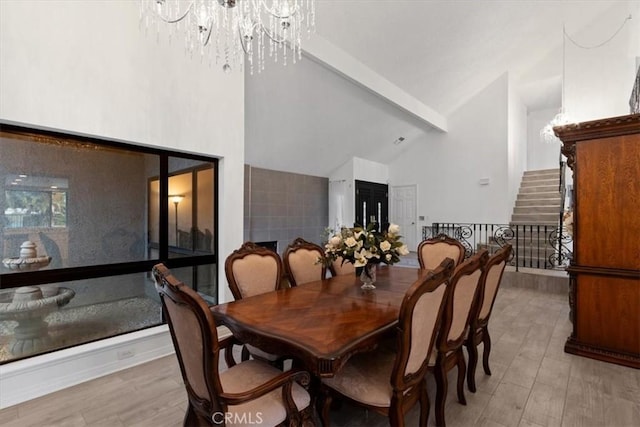 dining area with stairs, high vaulted ceiling, light wood-style floors, and an inviting chandelier