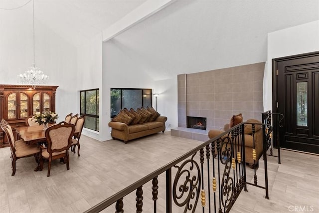 interior space with beam ceiling, a tiled fireplace, an inviting chandelier, light wood-style floors, and high vaulted ceiling