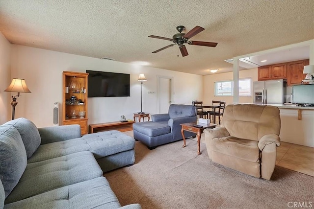 living area with ceiling fan, a textured ceiling, and light colored carpet