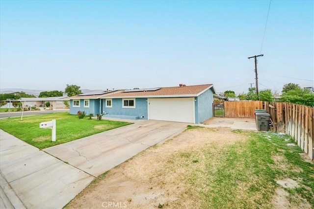 ranch-style house featuring solar panels, fence, concrete driveway, stucco siding, and a front yard