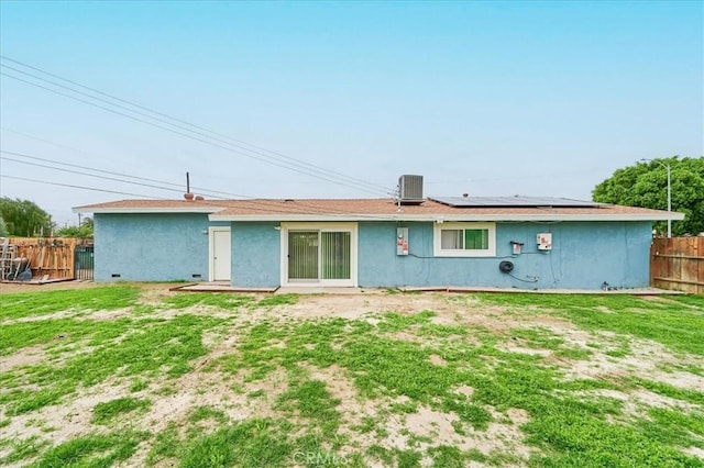 rear view of property with stucco siding, a lawn, roof mounted solar panels, central AC, and fence