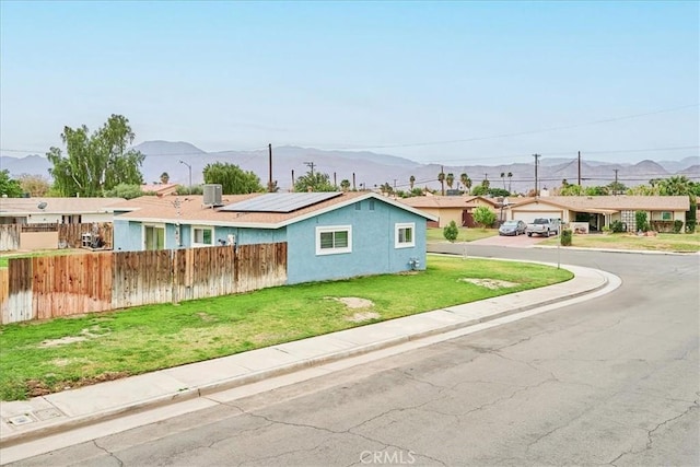 single story home with stucco siding, solar panels, a mountain view, fence, and a front lawn