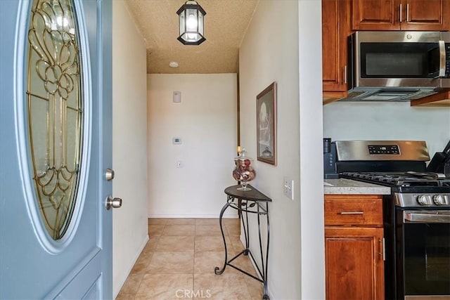 kitchen with stainless steel appliances, brown cabinetry, a textured ceiling, and light tile patterned floors