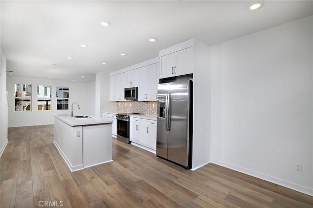 kitchen with white cabinets, appliances with stainless steel finishes, a sink, decorative backsplash, and light wood-type flooring