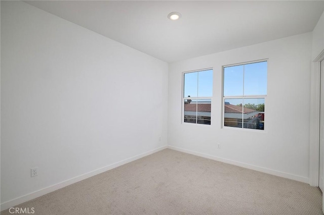 spare room featuring light colored carpet, recessed lighting, and baseboards