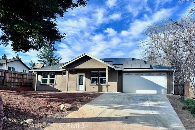 ranch-style home featuring solar panels, stucco siding, fence, a garage, and driveway