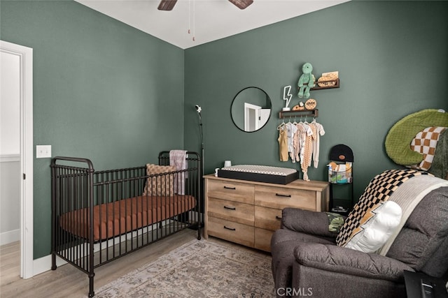 bedroom featuring ceiling fan, a crib, wood finished floors, and baseboards