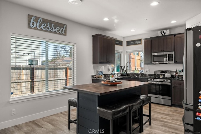 kitchen featuring stainless steel appliances, light wood-style floors, dark brown cabinetry, and a sink