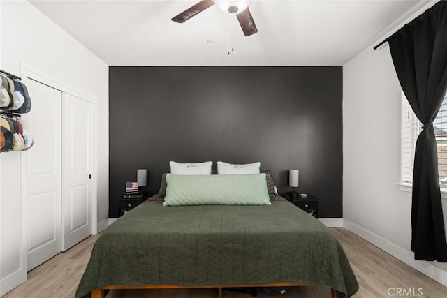 bedroom featuring ceiling fan, a closet, light wood-style flooring, and baseboards