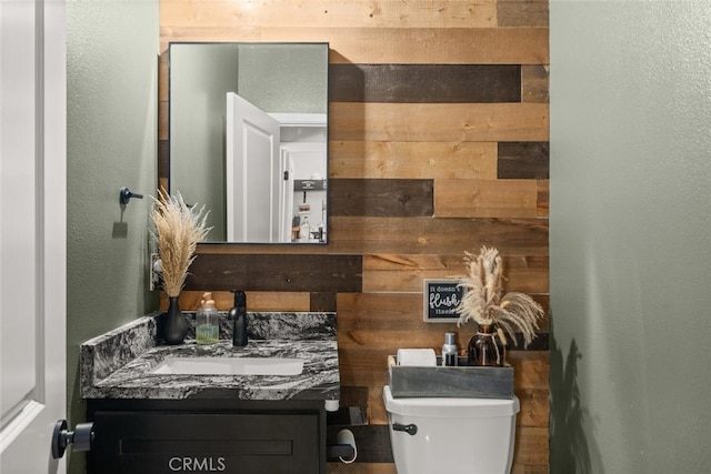 half bathroom with toilet, a textured wall, and vanity