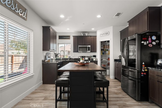 kitchen with light wood-style flooring, stainless steel appliances, a sink, visible vents, and dark brown cabinets