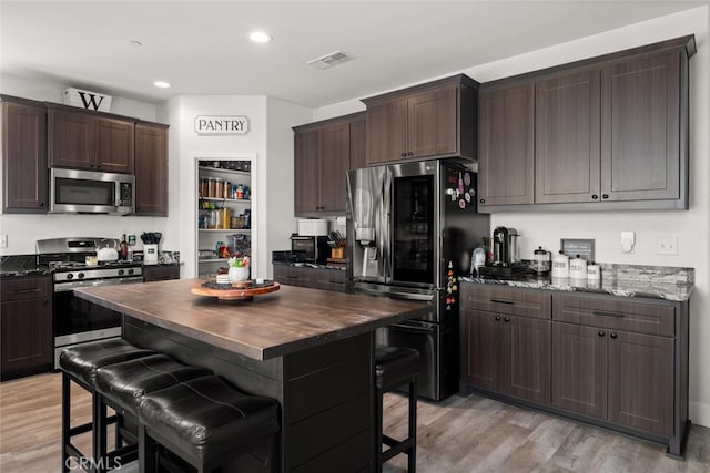 kitchen featuring dark brown cabinetry, visible vents, a kitchen breakfast bar, light wood-style floors, and appliances with stainless steel finishes