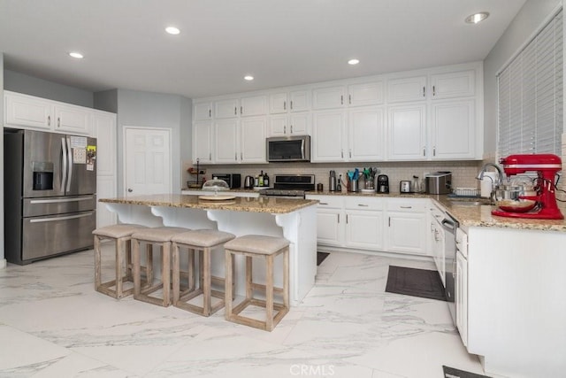 kitchen with light stone counters, white cabinetry, marble finish floor, appliances with stainless steel finishes, and backsplash