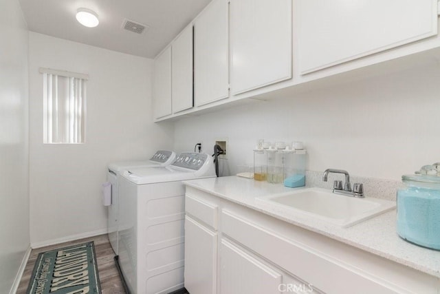 clothes washing area featuring cabinet space, visible vents, washer and clothes dryer, wood finished floors, and a sink