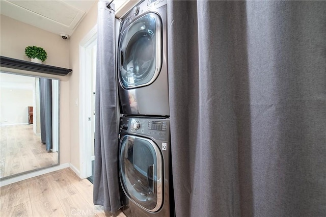 clothes washing area with laundry area, stacked washing maching and dryer, light wood-type flooring, and baseboards