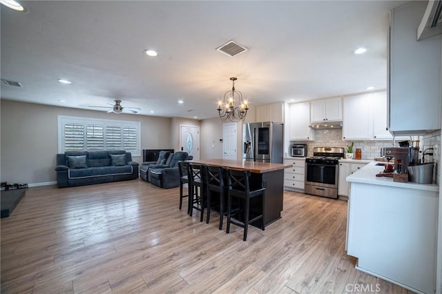 kitchen featuring visible vents, a kitchen bar, decorative backsplash, appliances with stainless steel finishes, and light wood-style floors