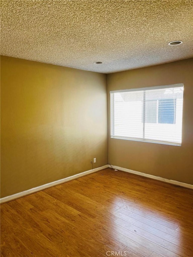 spare room featuring wood-type flooring, baseboards, and a textured ceiling