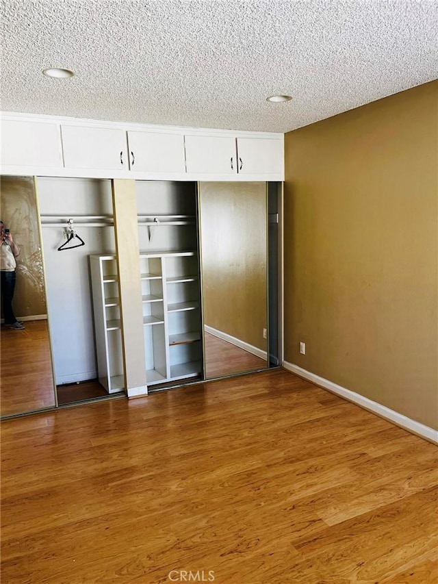 unfurnished bedroom with a textured ceiling, baseboards, and wood finished floors