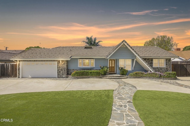 view of front facade with concrete driveway, an attached garage, a front yard, fence, and stone siding