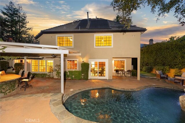 back of house at dusk with french doors, stucco siding, roof mounted solar panels, a patio area, and ceiling fan