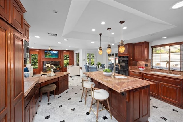 kitchen with a breakfast bar, a tray ceiling, dobule oven black, visible vents, and a sink