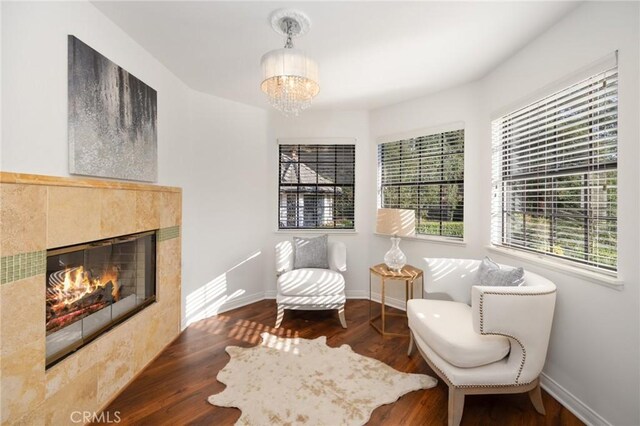 sitting room with a notable chandelier, baseboards, a tiled fireplace, and wood finished floors