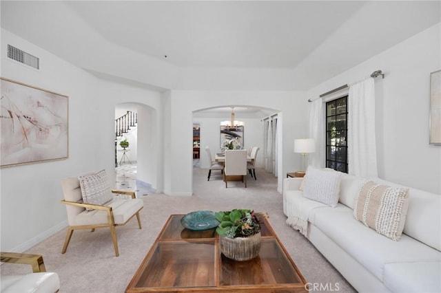 living room featuring carpet floors, arched walkways, visible vents, an inviting chandelier, and stairs