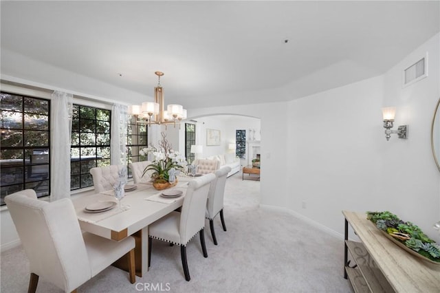 dining space featuring arched walkways, visible vents, light carpet, a chandelier, and baseboards