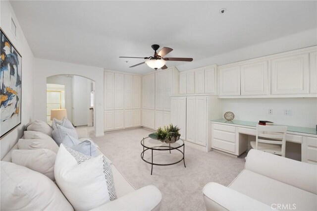 living area with visible vents, arched walkways, built in study area, and light colored carpet