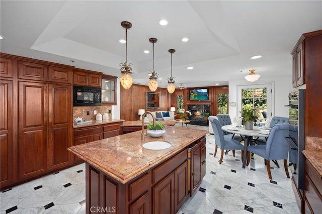 kitchen with light stone counters, a sink, open floor plan, a lit fireplace, and black appliances