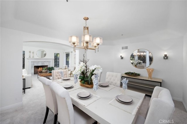 dining area featuring baseboards, visible vents, light colored carpet, a premium fireplace, and a chandelier