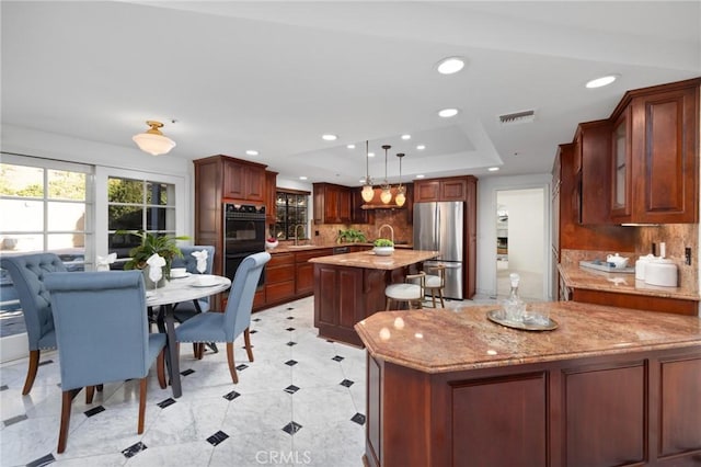 kitchen featuring light stone counters, a kitchen island, visible vents, freestanding refrigerator, and a tray ceiling