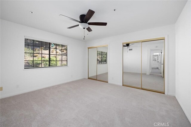 unfurnished bedroom featuring a ceiling fan, two closets, and carpet flooring