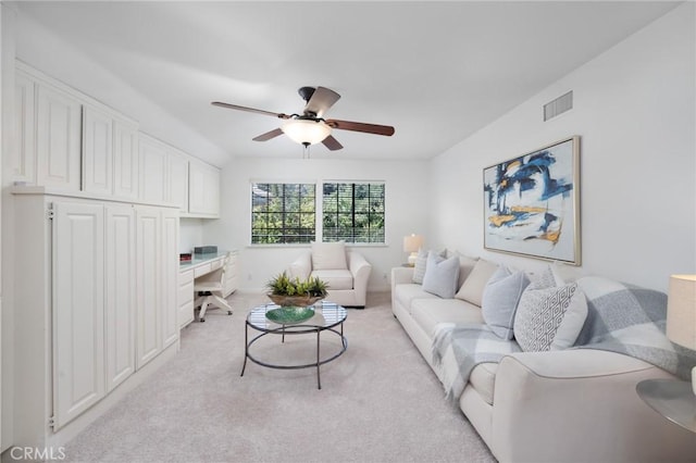 living room with ceiling fan, built in desk, visible vents, and light colored carpet