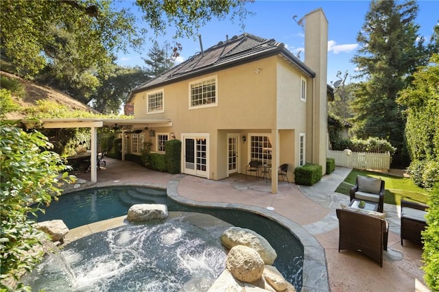 rear view of property with a chimney, stucco siding, a hot tub, a patio area, and fence