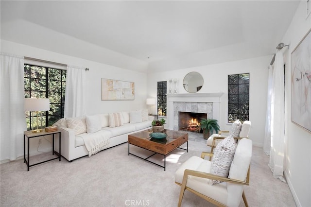 carpeted living area with baseboards, a tiled fireplace, a raised ceiling, and a healthy amount of sunlight