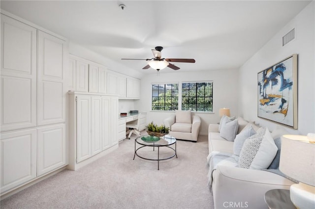 living area with light carpet, visible vents, a ceiling fan, and built in study area