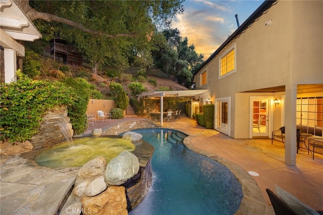 pool at dusk featuring a pool with connected hot tub and a patio