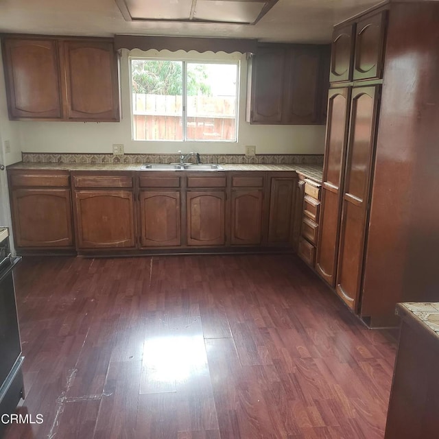 kitchen with a sink, brown cabinetry, light countertops, and dark wood-style flooring