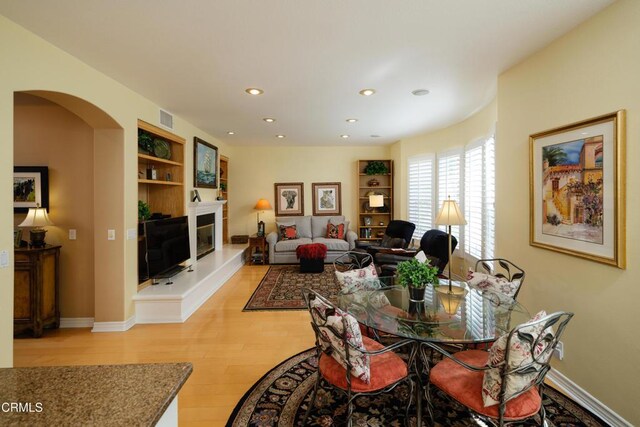 dining area featuring arched walkways, built in shelves, light wood-style flooring, visible vents, and a glass covered fireplace