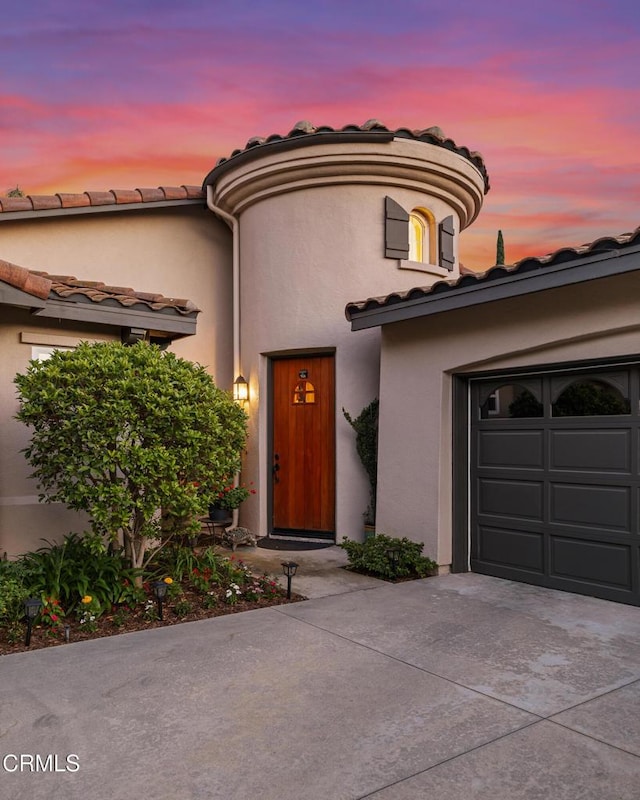 view of front facade with driveway, an attached garage, a tiled roof, and stucco siding