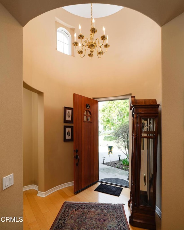 foyer with light wood-style floors, a high ceiling, baseboards, and an inviting chandelier