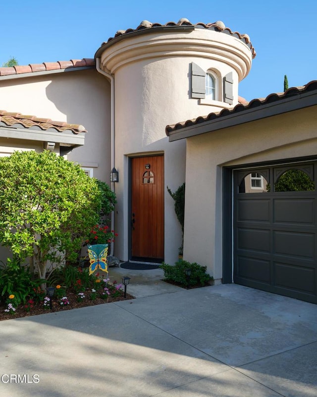 view of exterior entry featuring a garage, driveway, a tiled roof, and stucco siding