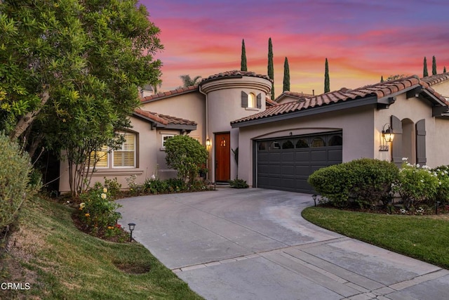 mediterranean / spanish-style house with a yard, stucco siding, an attached garage, driveway, and a tiled roof