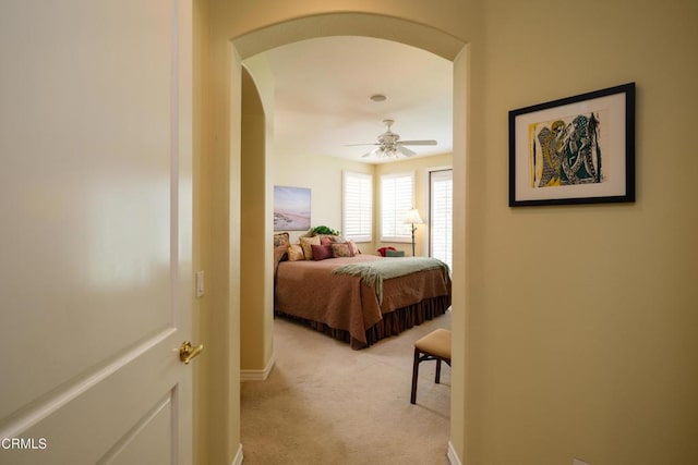 bedroom with a ceiling fan, arched walkways, light carpet, and baseboards